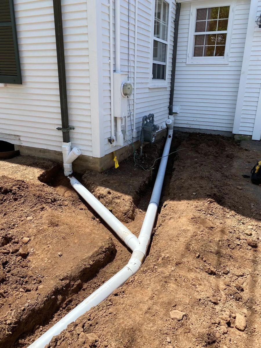 New white PVC drain lines laid in a trench beside a house